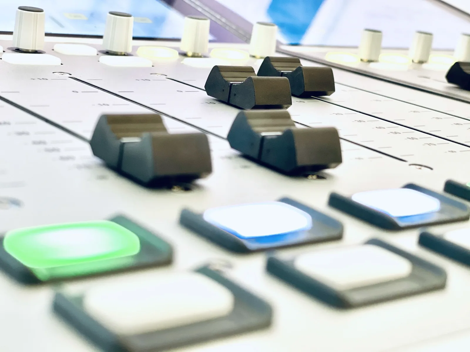 Detailaufnahme eines Audiomischpults mit Fadern und beleuchteten Tasten